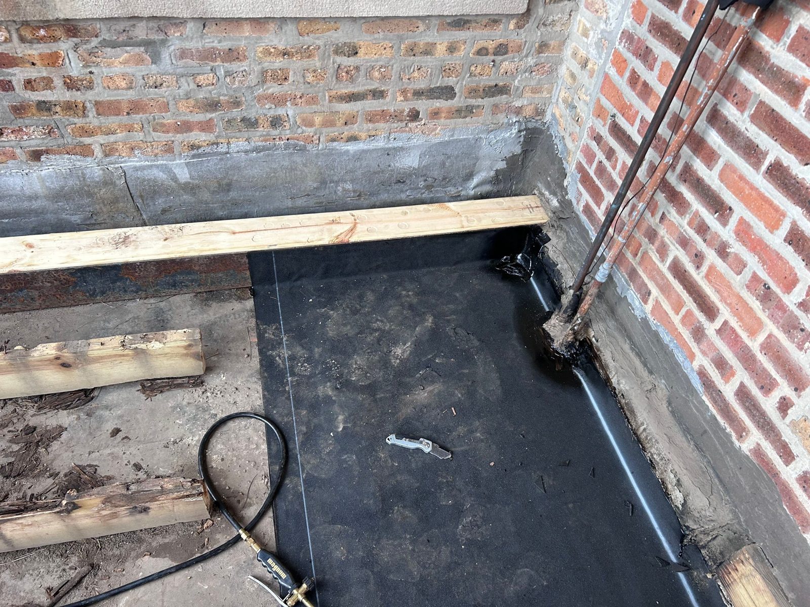 Concrete deck waterproofing membrane sealed at brick corner.