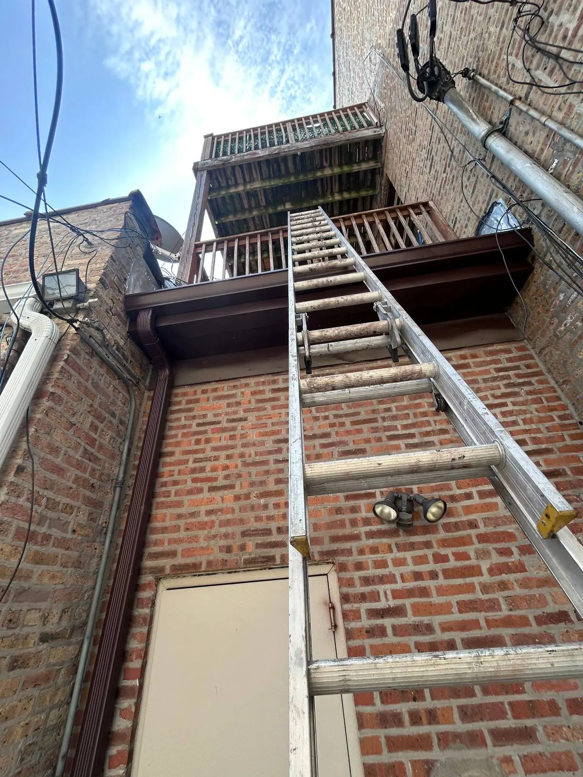 Gutter and downspout connection on a multi-story brick facade with ladder access.