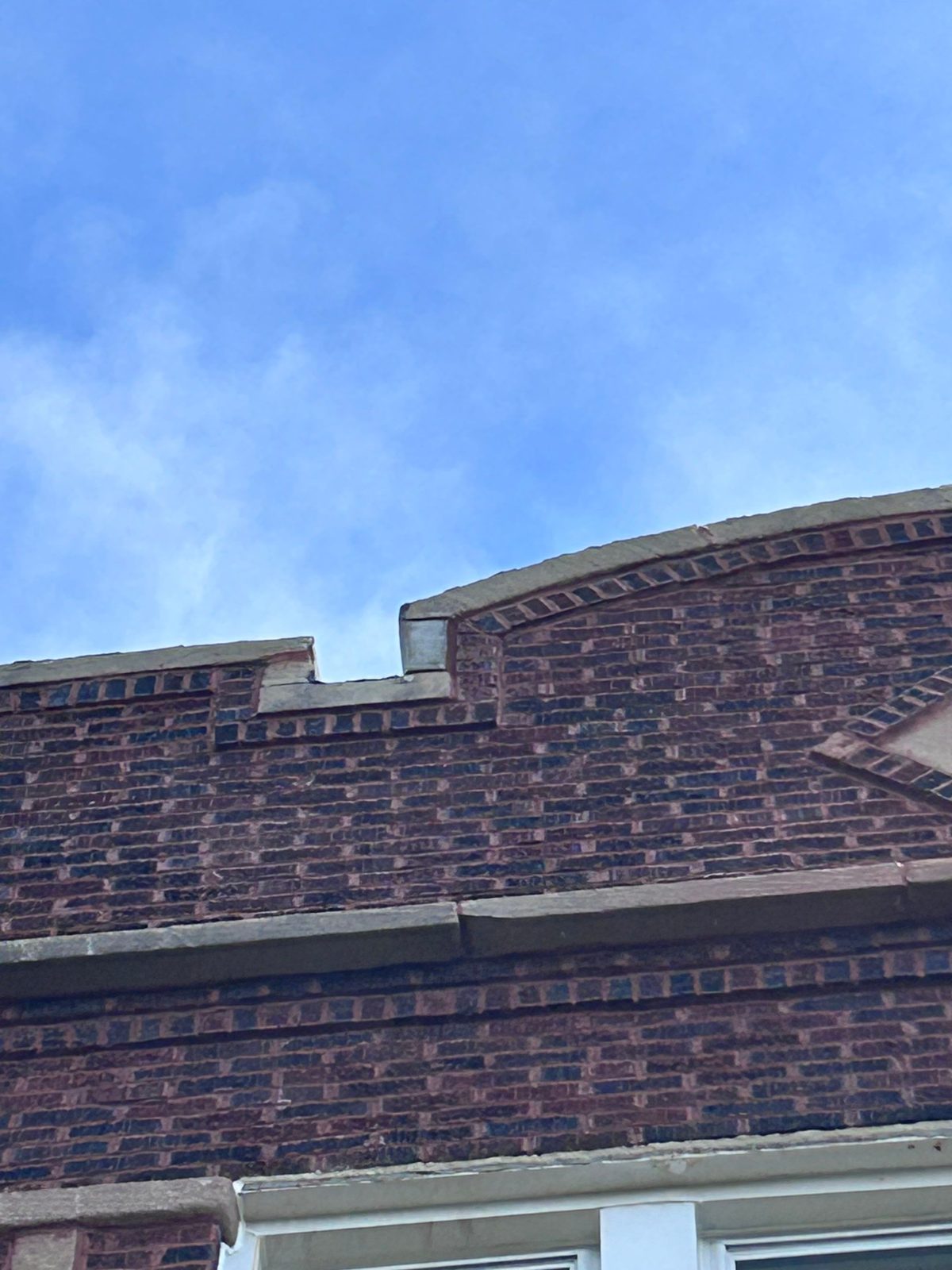 Dark brick parapet with decorative banding and stone coping against blue sky.