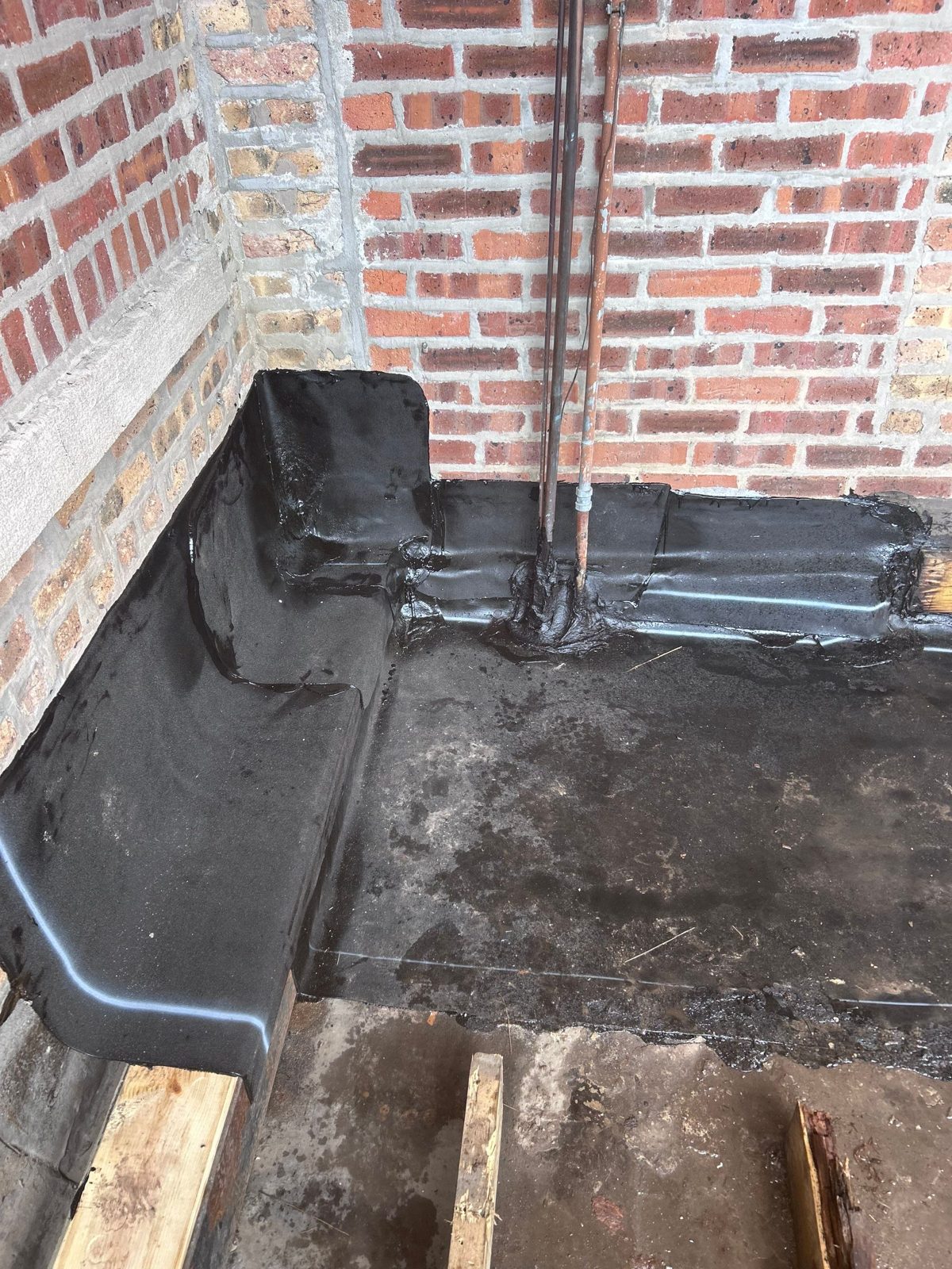 Black waterproofing applied at the base of a red brick wall.