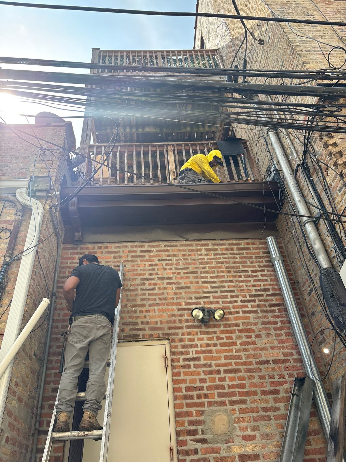 Crew on ladder and balcony working brick facade exterior.