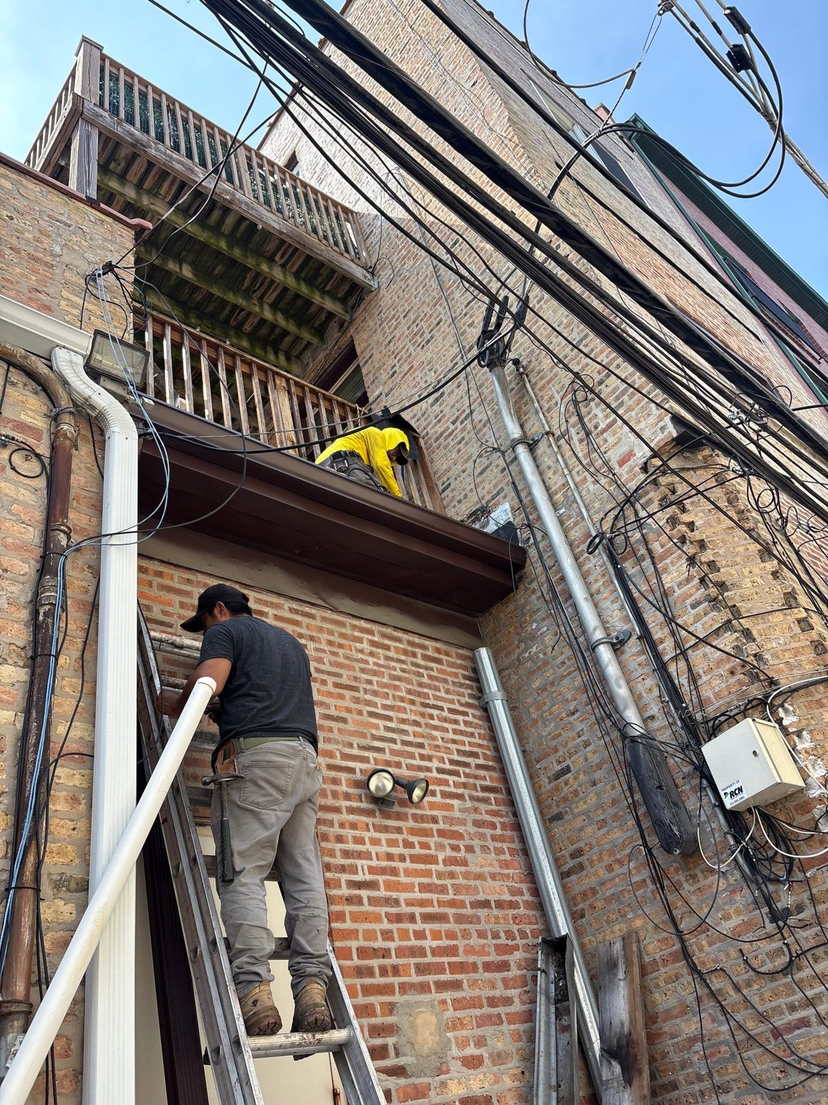 Crew on ladder accessing multi-story brick facade for exterior repair.