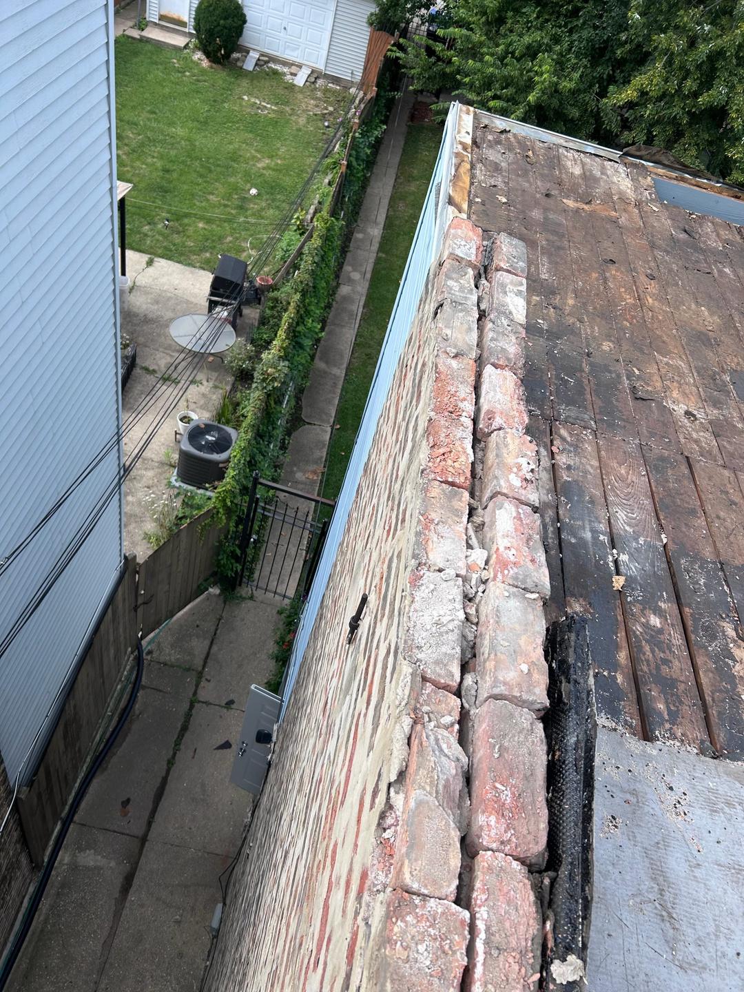 Before: deteriorated brick parapet with loose, crumbling top courses running along a flat roof torn off down to the wood deck.