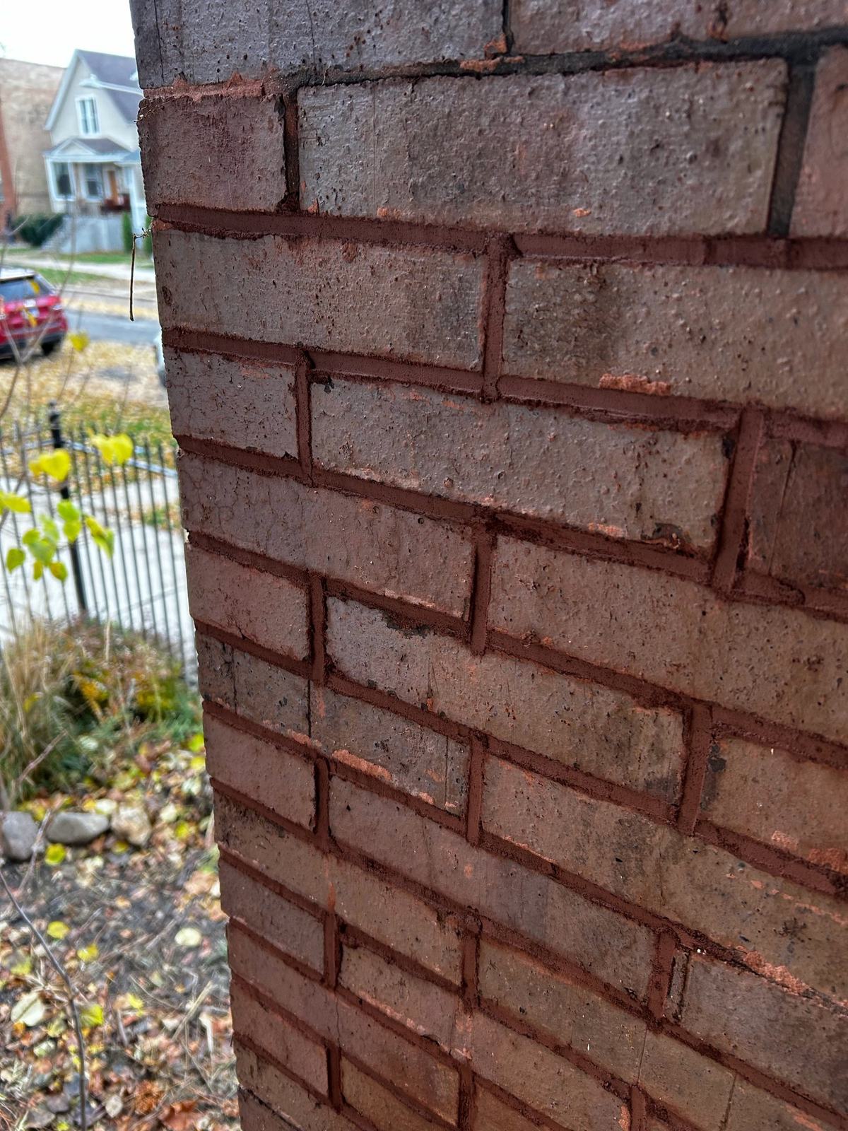 Close-up of finished tuckpointing: new reddish mortar joints tooled neatly between the bricks of a porch column.