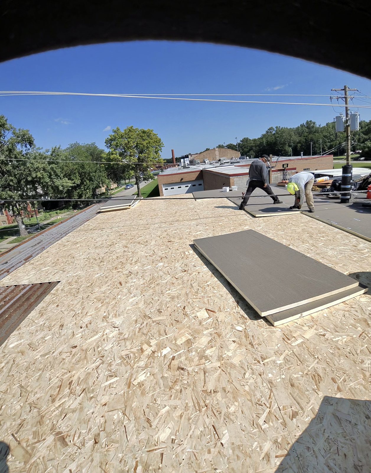 Crew installing rigid insulation boards over new OSB deck on a flat roof.