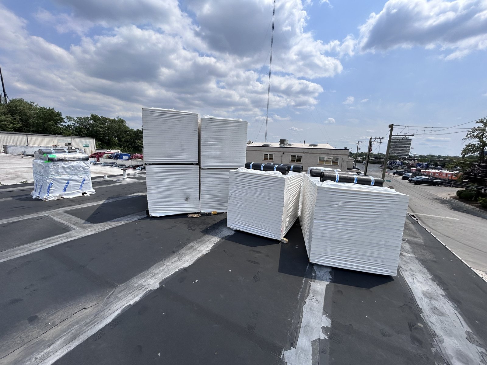 Stacks of insulation boards and Soprema modified bitumen rolls staged on a flat roof.