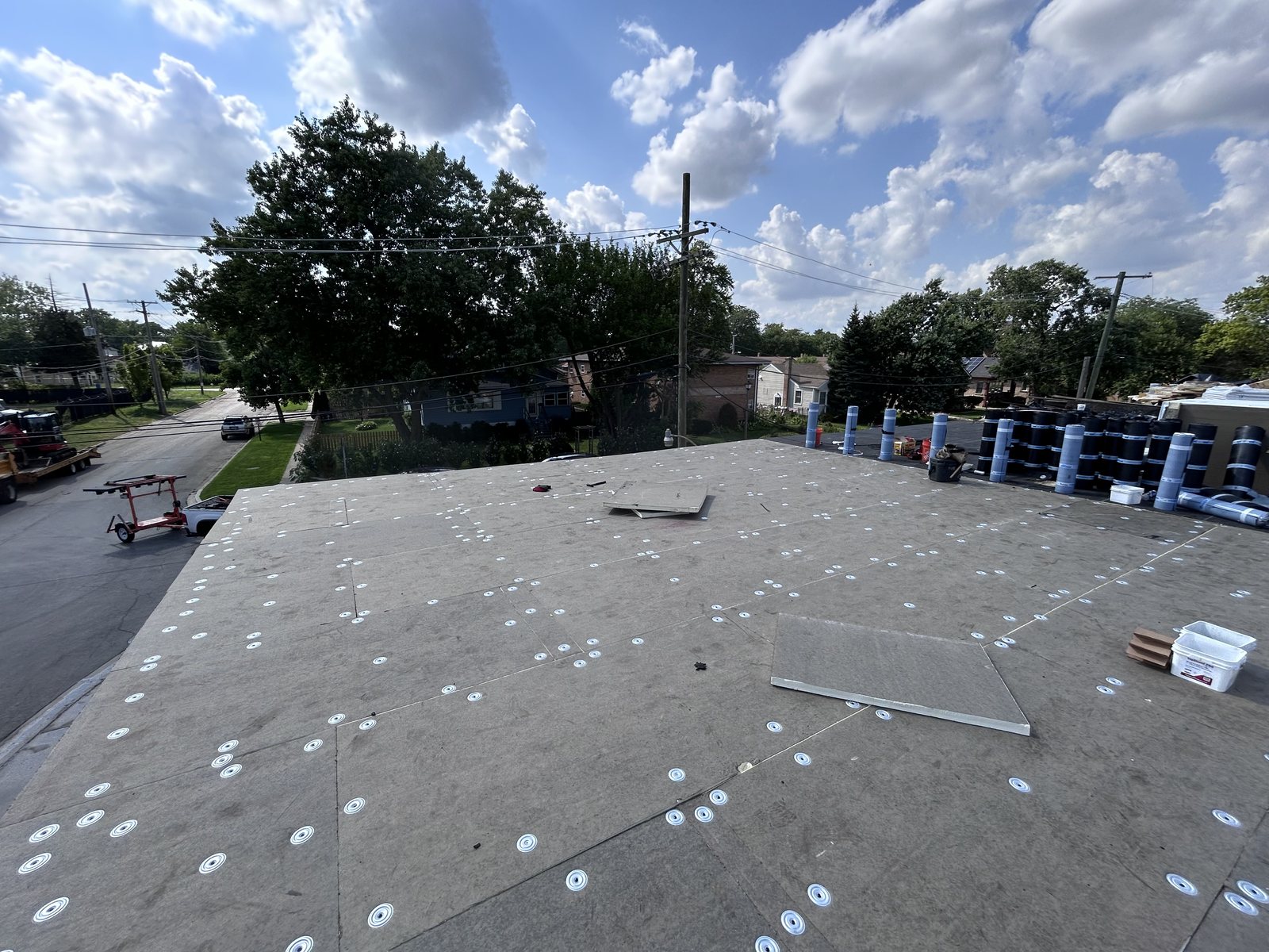 Cover board secured with fastener plates and modified bitumen rolls staged for install.