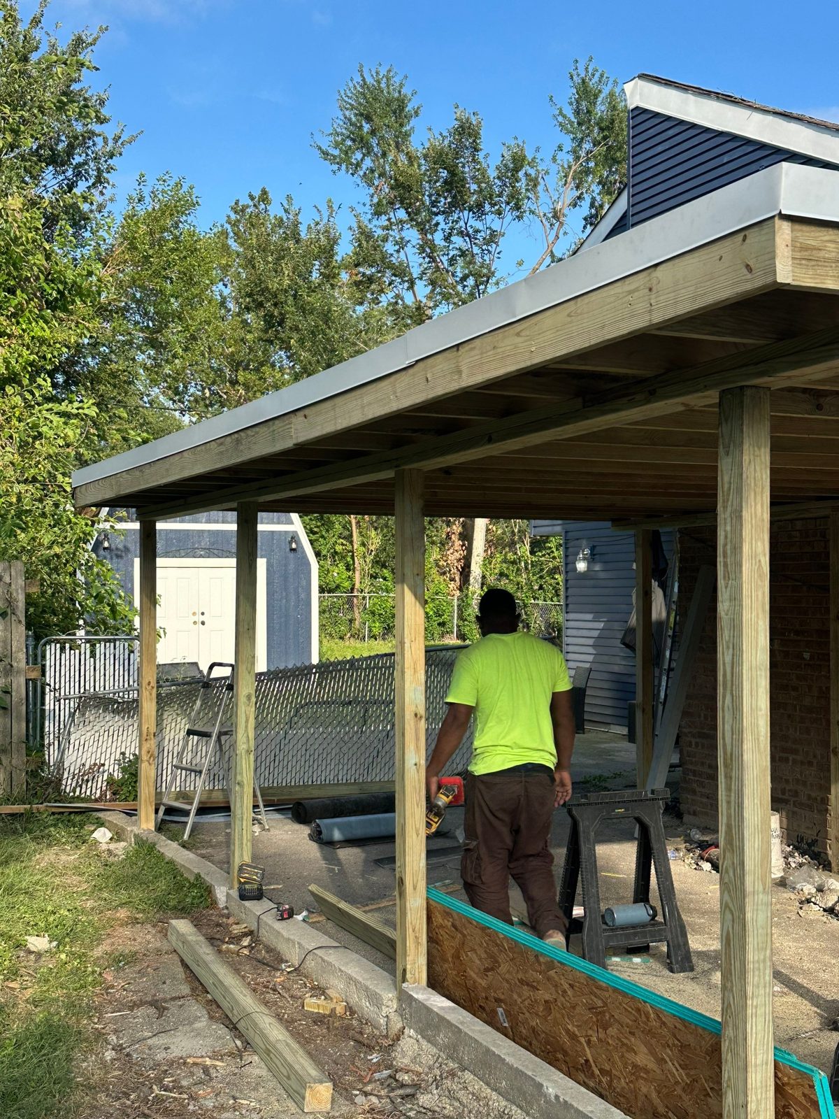 Worker framing a new porch roof with PT lumber and metal edge trim.